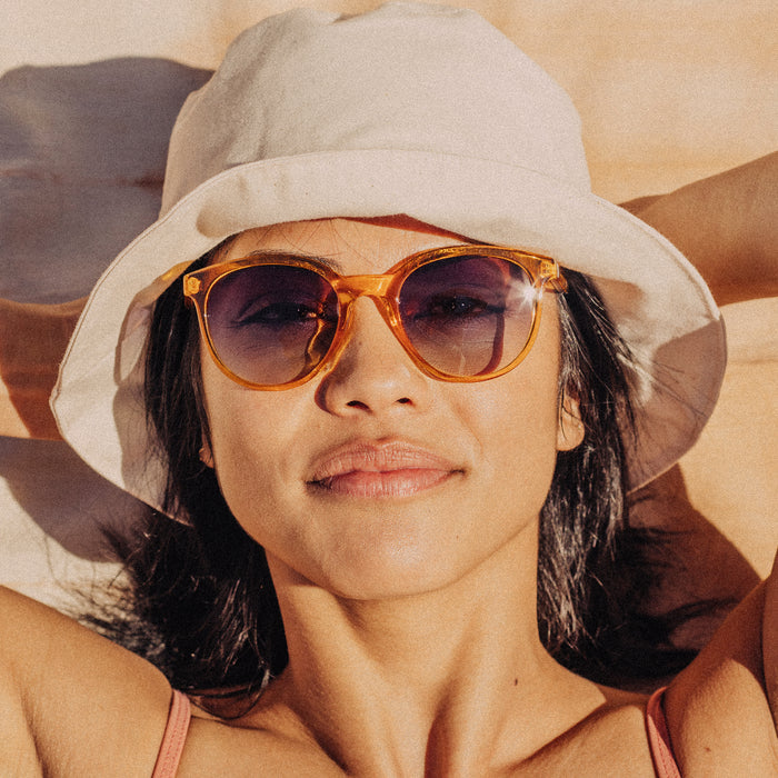 Woman wearing a beige hat and sunglasses with a blurred natural background