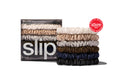 A collection of Slip silk skinny scrunchies in white, silver, blonde, navy, dark brown, and black, stacked and displayed in branded packaging on a white background.