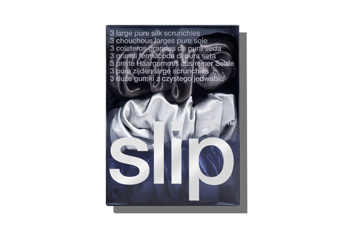 A set of three slip silk large scrunchies in navy, silver, and charcoal, displayed in branded packaging on a white background.