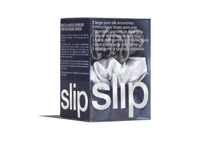 A set of three slip silk large scrunchies in navy, silver, and charcoal, displayed in branded packaging on a white background.