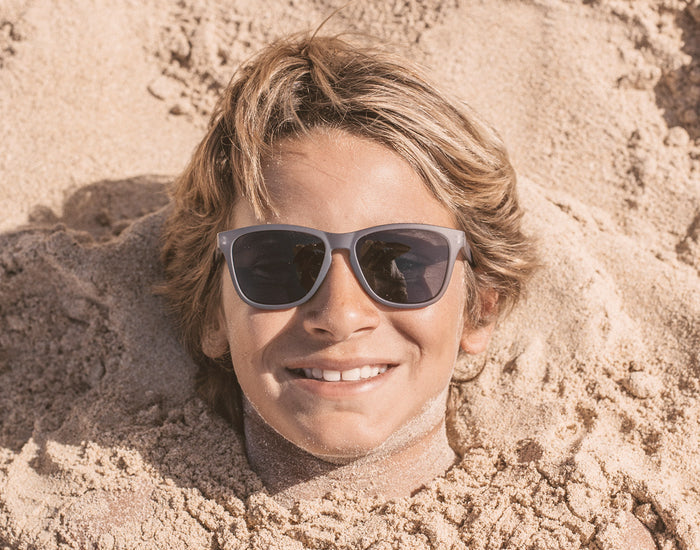 STORY boy buried in the sand wearing sunski mini headland sunglasses