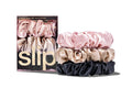 A set of three slip silk large scrunchies in pink, caramel, and black stacked, and in a branded box on a white background.