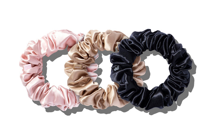 A set of three slip silk large scrunchies in pink, caramel, and black stacked on a white background.