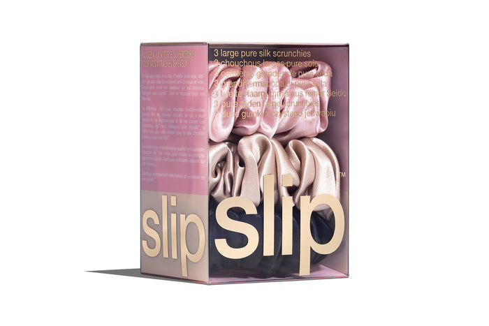 A set of three slip silk large scrunchies in pink, caramel, and black in a branded box on a white background.