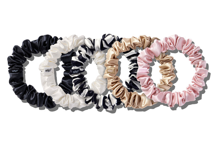 A set of five Slip silk midi scrunchies in various colors including black, pink, caramel, white, and navy stripe on a white background.