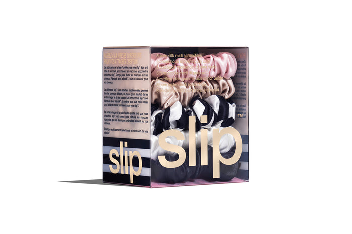 A set of five Slip silk midi scrunchies in various colors including black, pink, caramel, white, and navy stripe in branded packaging on a white background.