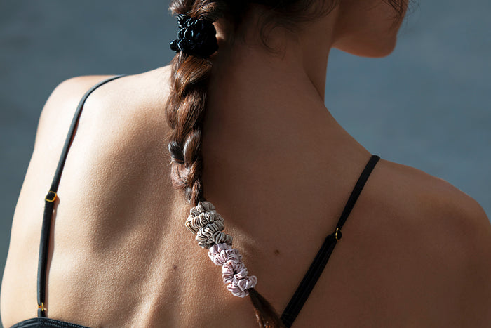 A woman with a styled braid with slip silk skinny scrunchies in black, caramel and pink.