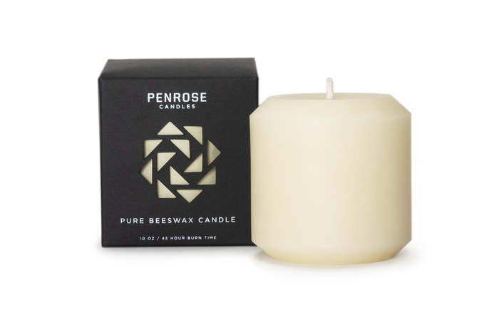 A natural 3 inch  ivory pillar candle next to its black packaging box with a geometric pattern, labeled as 'Penrose Pure Beeswax Candle'.