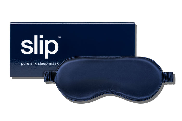 A navy slip silk sleep mask displayed with branded packaging on a white background.