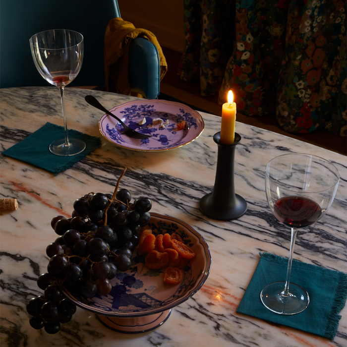 Marble table set with wine glasses, cloth napkins, candlelight and Ginori porcleain pieces with floral motifs and gold accents.