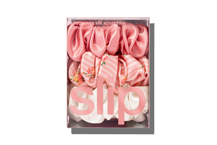 Stack of pink, floral pattern and white large slip silk scrunchies, displayed in branded packaging on a white background.