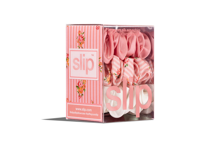 Stack of pink, floral pattern and white large slip silk scrunchies, displayed in branded packaging on a white background.