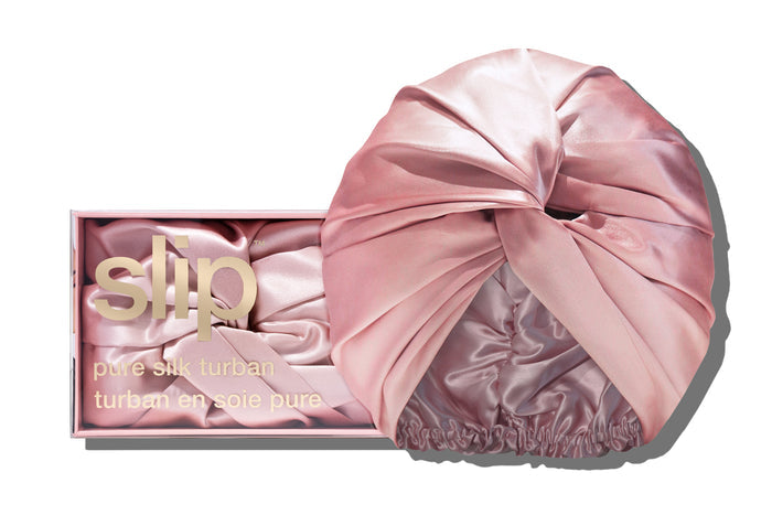 A pink slip silk turban in front of with branded packaging on a white background.