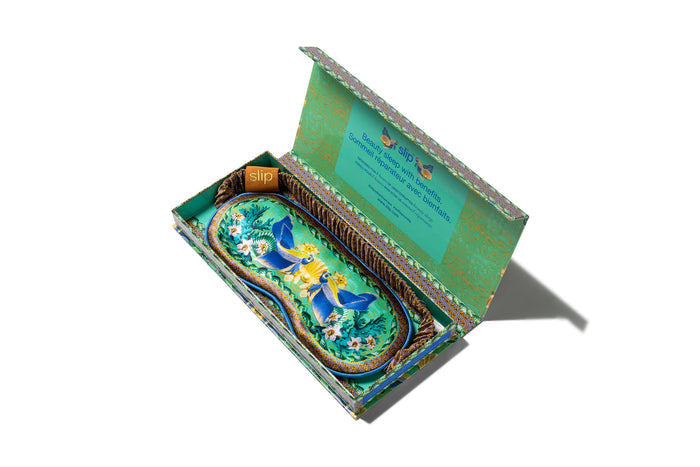 A floral and fish patterned slip silk sleep mask for Pisces star sign with blue, green, and brown colors. Displayed inside an open branded box on a white background.