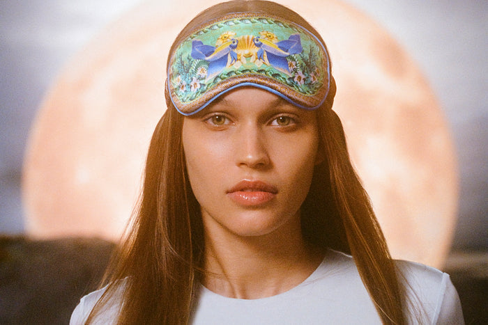 A woman wearing a floral and fish patterned slip silk sleep mask for Pisces star sign with blue, green, and brown colors.