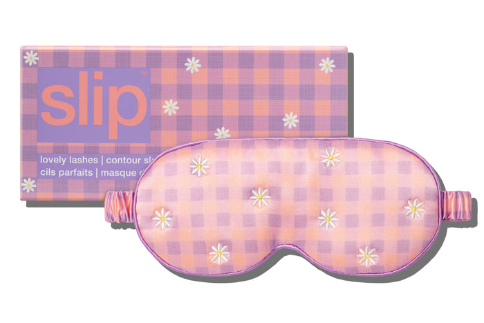A slip silk contour sleep mask with a pink and purple checkered pattern and embroidered daisies, designed for eyelash extension wearers. Displayed alongside slip packaging on a white background.
