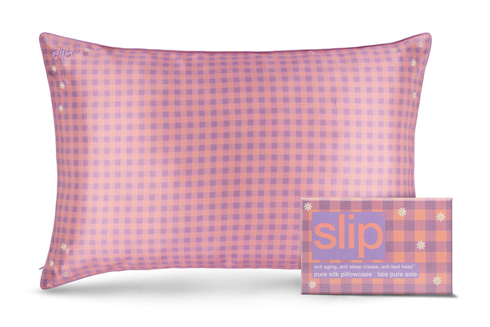 A slip silk queen pillowcase with a pink and purple checkered pattern and embroidered daisies, displayed alongside its slip packaging on a white background.