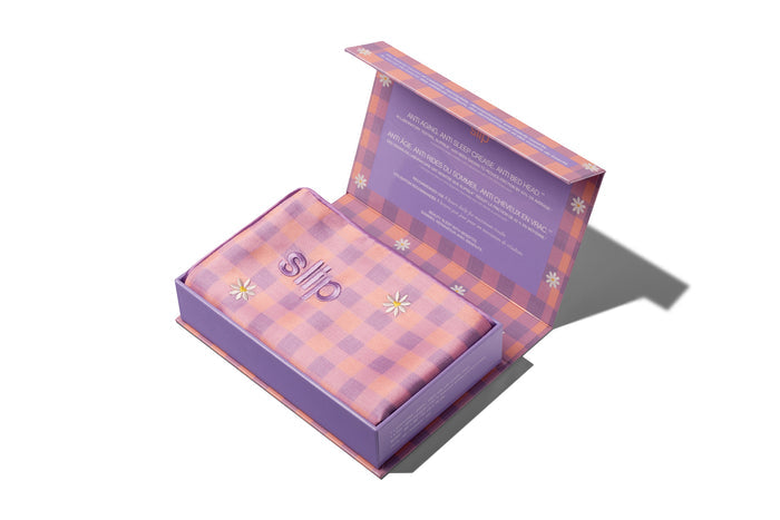 A slip silk queen pillowcase with a pink and purple checkered pattern and embroidered daisies, displayed in open lid slip packaging on a white background.