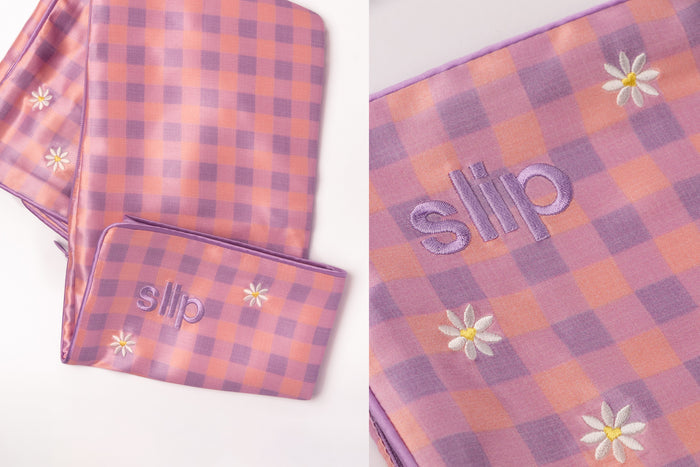 A close up of a slip silk queen pillowcase with a pink and purple checkered pattern with embroidered daisies.