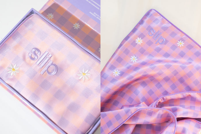 A slip silk queen pillowcase with a pink and purple checkered pattern with embroidered daisies.