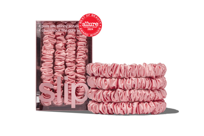 A set of four blush pink silk skinny scrunchies displayed in a box and stacked in front with a allure award badge on a white background