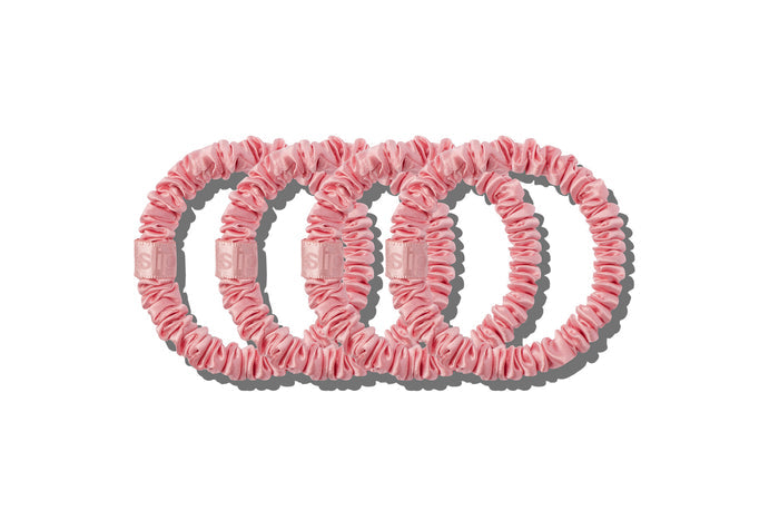 Four blush pink silk skinny scrunchies on a white background