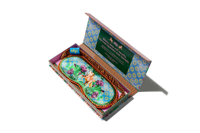 A slip silk sleep mask with a floral and horse pattern in open packaging box on a white background.