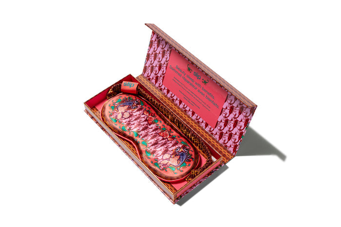 A slip Scorpio silk sleep mask with a scorpion pattern, predominantly in pink, red and purple shades  in open packaging box on a white background.