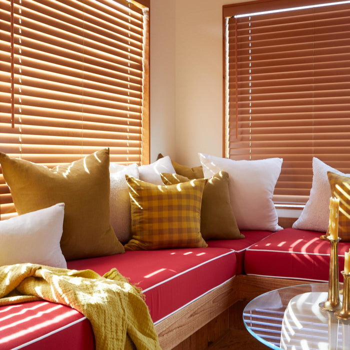 Red sofa with colorful cushions in a room with wooden blinds.