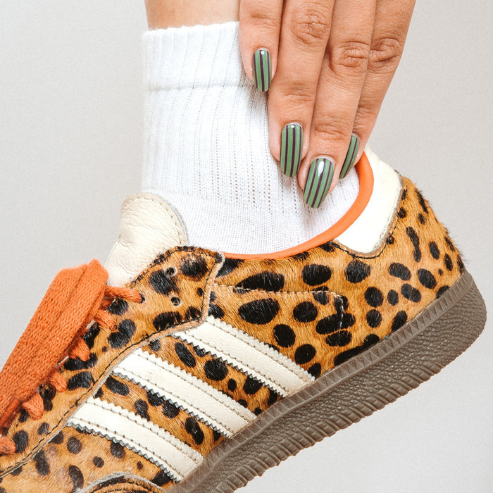 Close-up of Stripe Tease gel nail stickers by Maniac Nails above a leopard print sneaker