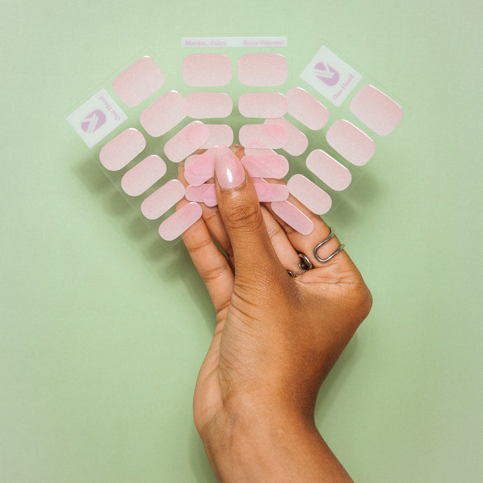 Hands holding Sugar Shimmer gel nail sticker sheets by Maniac Nails on a green background
