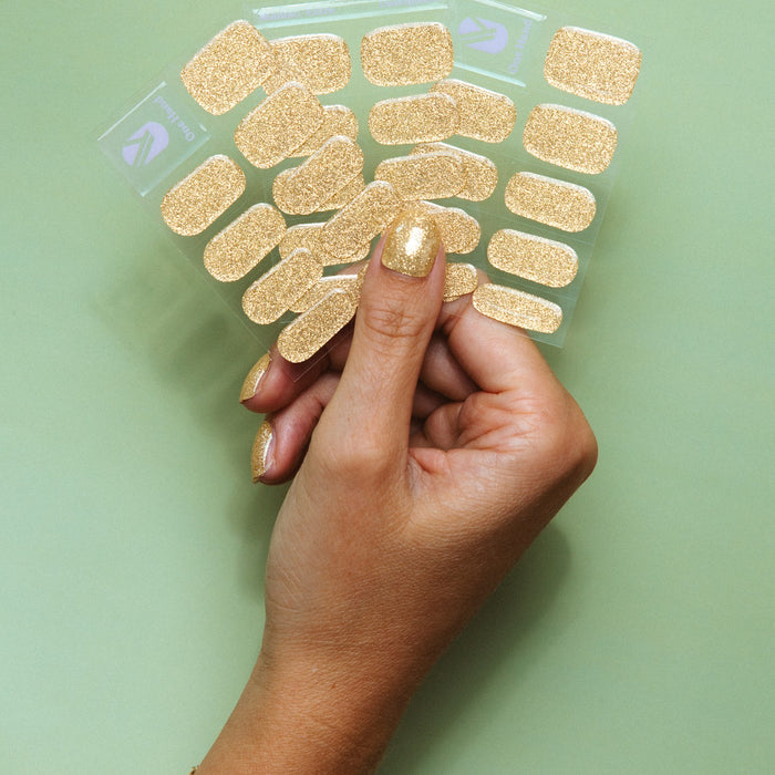 Hand holding Unstoppable gold glitter gel nail sticker sheets by Maniac Nails