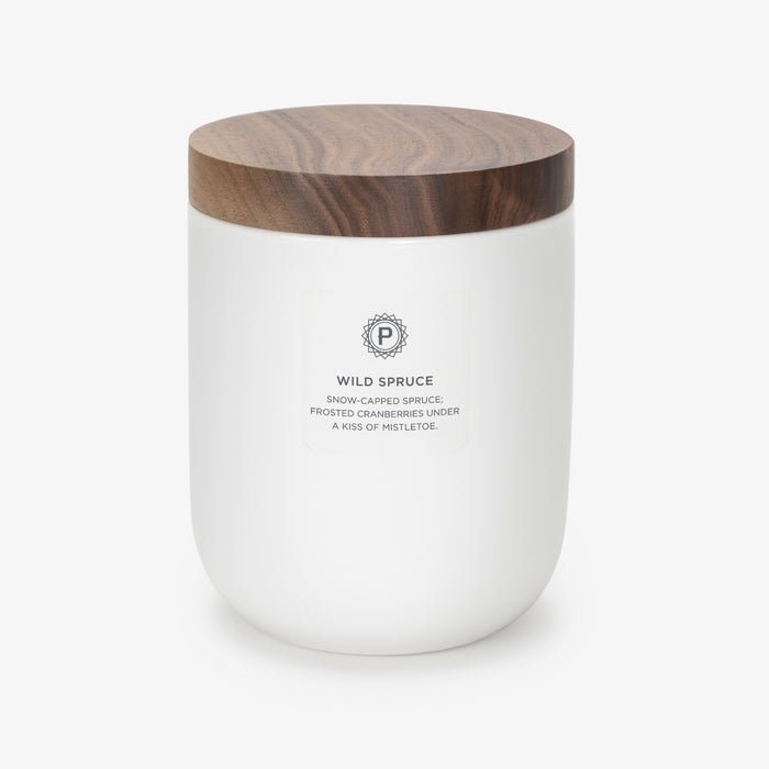 A white ceramic candle with a walnut wooden lid, labeled 'WILD SPRUCE', with scents of spruce, fresh mint, and cranberry. 10.5 OZ
