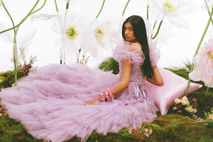 Woman resting arm on a lilac slip silk queen pillowcase in a lilac dress, wearing a slip silk large scrunchies.