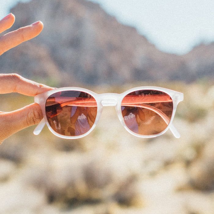 Sunglasses with red-tinted lenses held in front of a blurred natural background